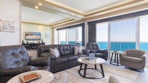 A modern living room with a leather sofa, armchairs, a coffee table, and a large window with a view of the ocean. - Splash in The New Lazy River and Sleep In Luxury Encantame Towers C 1204 (Puerto Peñasco)