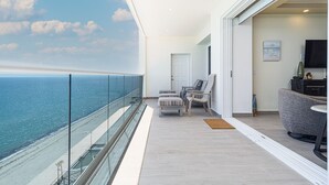 A balcony with a view of the ocean, a seating area with chairs and a sofa, and a television on the right. - Splash in The New Lazy River and Sleep In Luxury Encantame Towers C 1204 (Puerto Peñasco)