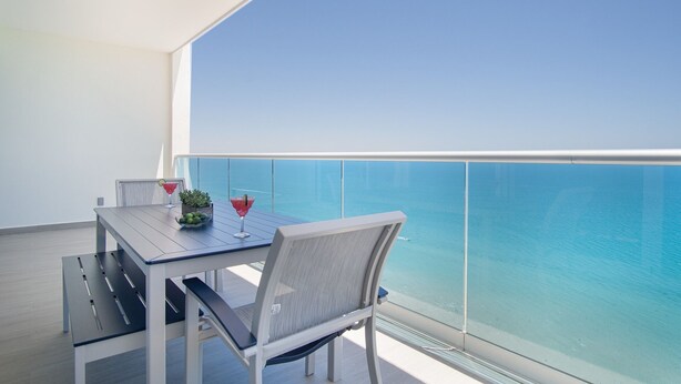 A balcony with a table and chairs, a glass railing, and a view of the ocean. - Splash in The New Lazy River and Sleep In Luxury Encantame Towers Velero 2104 (Puerto Peñasco)