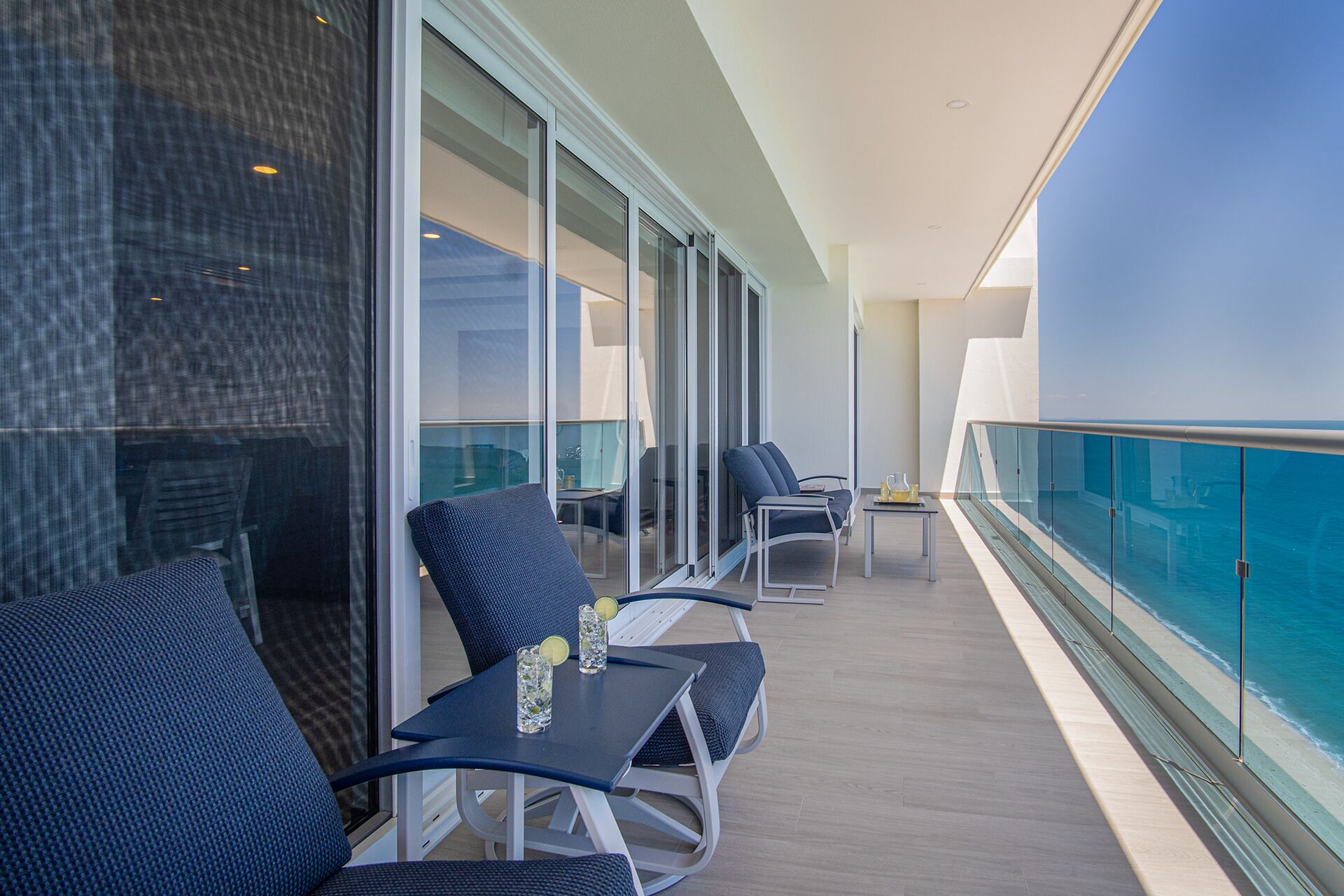 A balcony with outdoor seating and a glass railing overlooking the ocean.