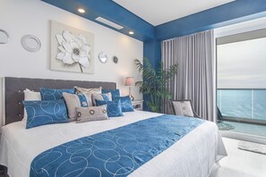 Een moderne slaapkamer met een groot bed, een decoratief wandobject en uitzicht op de oceaan.