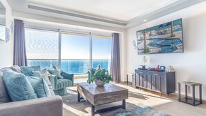 A spacious living room with a large window, a sofa set, a coffee table, and a painting on the wall.