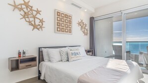A bedroom with a large bed, a nightstand, and a view of the ocean through a sliding glass door.