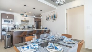 A modern kitchen with stainless steel appliances, a dining area with a glass table set for six, and a decorative wall art piece.