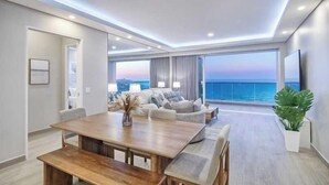 Una sala de estar moderna con una mesa de comedor de madera, sofás y un ventanal con vista al mar.