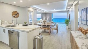 Una cocina moderna con una isla central, un comedor con vistas al océano y una sala de estar con un amplio ventanal que da al mar.