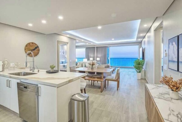 A modern kitchen with a central island, a dining area with a view of the ocean, and a living space with a large window overlooking the sea.