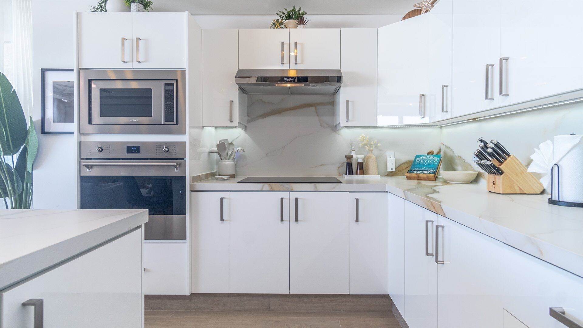 A modern kitchen with white cabinetry, stainless steel appliances, and a marble countertop.