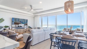 A spacious living area with a large window overlooking the sea, a dining area with a view, and a ceiling fan.