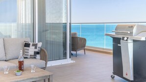 A balcony with a grill, a sofa with cushions, and a table with glasses and a bottle.