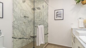 Une salle de bain moderne avec une douche à parois de verre, des murs en marbre et une œuvre d’art encadrée.