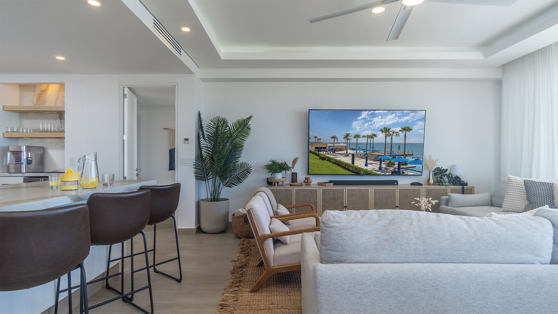 A modern living room with a large TV, a bar area, and a seating area with a sofa and chairs.