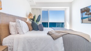 A modern hotel room with a large bed, a view of the ocean, and a balcony with a railing.