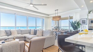 A modern living room with a large sectional sofa, a dining area, and a kitchen with a view of the ocean.