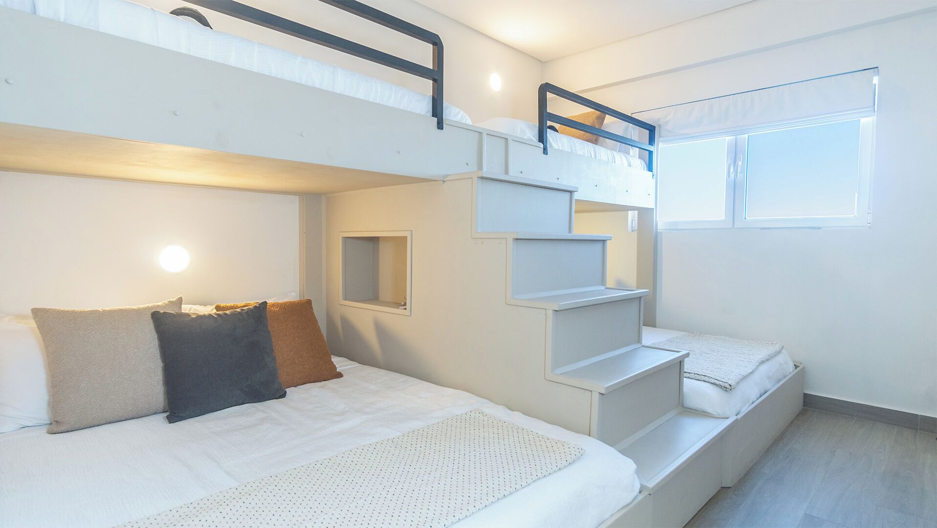 A bunk bed room with a small window, a mirror, and a white wall.
