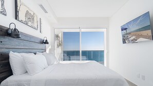 A bedroom with a large bed, a wooden headboard, a view of the sea through a glass door, and artwork on the walls. - Stay in Luxury/splash in New Lazy River This Winter Encanatame Towers 902 (Puerto Peñasco)