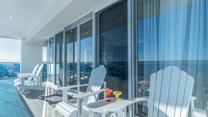 A balcony with white chairs and a glass partition, overlooking a cityscape. - Impressive & Beautiful 3 Bedroom Unit Ocean Front Encantame Velero-2301 (Puerto Peñasco)