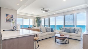 A spacious living area with a large window overlooking the ocean, a kitchen with a bar area, and a ceiling fan. - Amazing two Bedroom Beach Front Condo W405 (Puerto Peñasco)