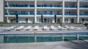 A modern hotel with a pool area featuring sun loungers and umbrellas, a multi-story building with balconies, and a clear blue pool. - Splash in The New Lazy River/stay in Modern Luxury Encantame Viento 303 (Puerto Peñasco)