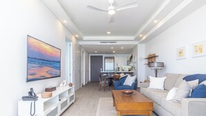 A spacious living area with a sofa, coffee table, and a painting of a sunset. - Encantame Towers Viento 1503 (Puerto Peñasco)