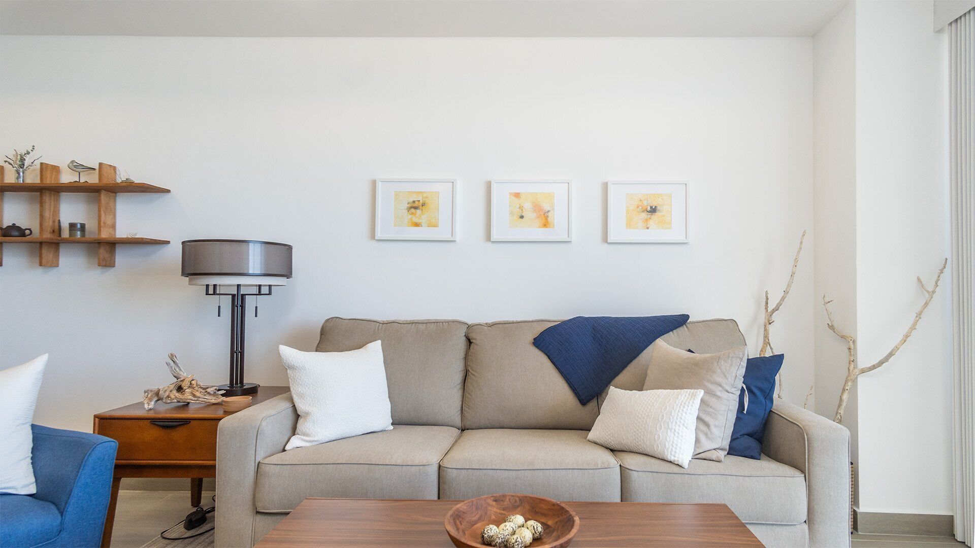 A living room with a sofa, a coffee table, a side table, and a lamp. There are three framed pictures on the wall.