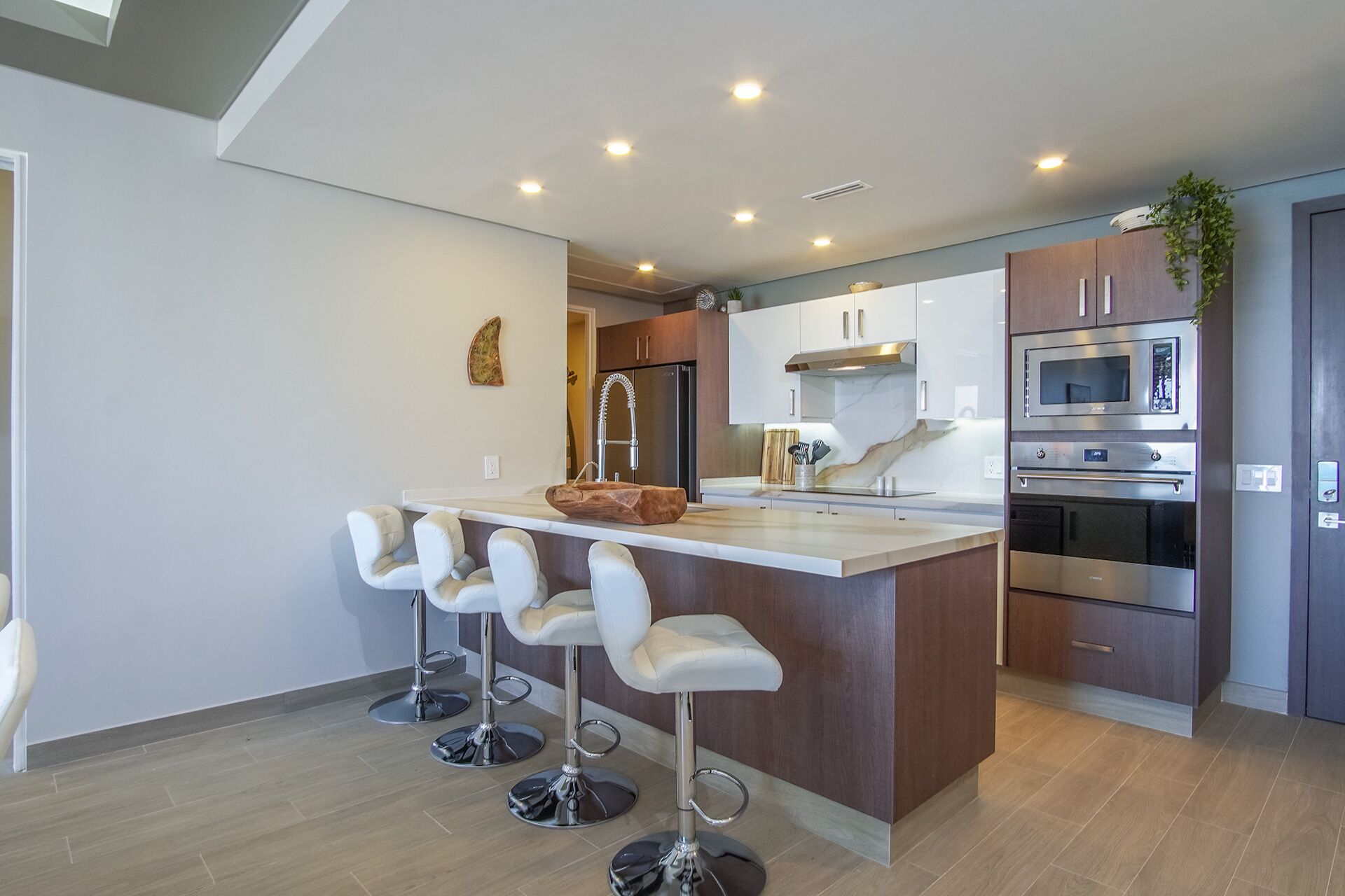 A modern kitchen with a central island, bar stools, stainless steel appliances, and wooden cabinets.