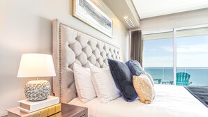 A hotel room with a large bed, a nightstand with a lamp, and a view of the ocean. - Lovely 2 Bedroom Condominium (Puerto Peñasco)