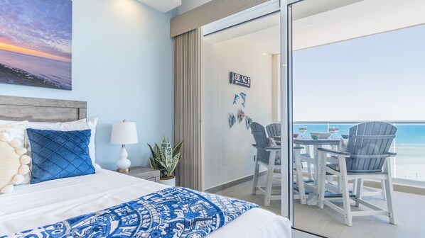 Ein Hotelzimmer mit einem Bett, einem Nachttisch, einer Lampe, einem Blumentopf und einem Balkon mit Tisch und Stühlen.