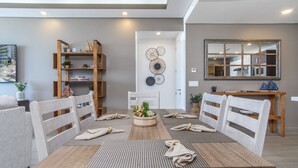 A modern dining area with a wooden table, white chairs, and a central island with a plant. - Perfect Family 2 Bedroom Condo Encantame Viento 504 (Puerto Peñasco)