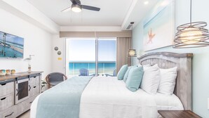 A bedroom with a large bed, a ceiling fan, a view of the ocean, and a dining area with a view. - Perfect Family 2 Bedroom Condo Encantame Viento 504 (Puerto Peñasco)