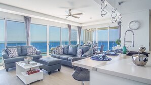 A modern living room with a large window overlooking the sea, a ceiling fan, and a dining area with a view.