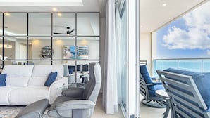 A modern living room with a sofa, chairs, and a glass coffee table. There is a large window with a view of the ocean. - Amaizing Condo by the Beach Encantame W1704 (Puerto Peñasco)