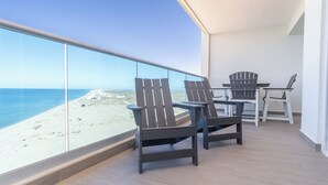 Un balcón con vistas a una playa y el océano, con dos sillas Adirondack y una mesita.