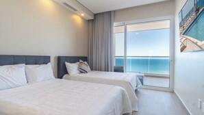 Habitación de hotel con dos camas, un ventanal con vista al océano y un cuadro en la pared.