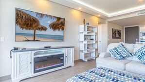 Una sala de estar con chimenea, un cuadro con motivos marinos, un sofá blanco con cojines azules y un estante blanco decorado con objetos.
