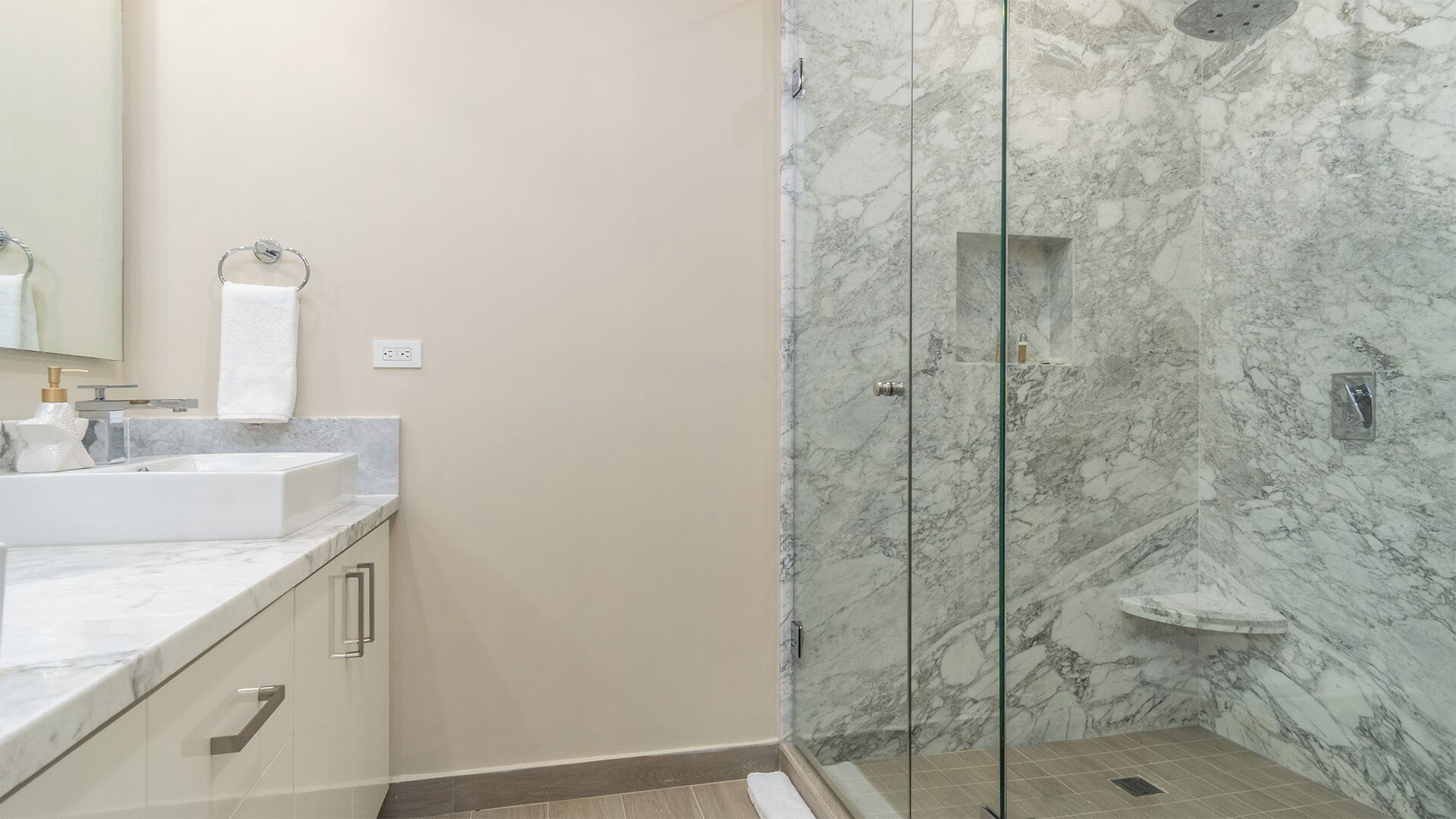 A modern bathroom with a marble shower, a sink, and a mirror.