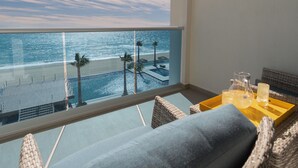 A balcony with a view of the beach and ocean, a seating area with cushions, and a tray with glasses and a pitcher.