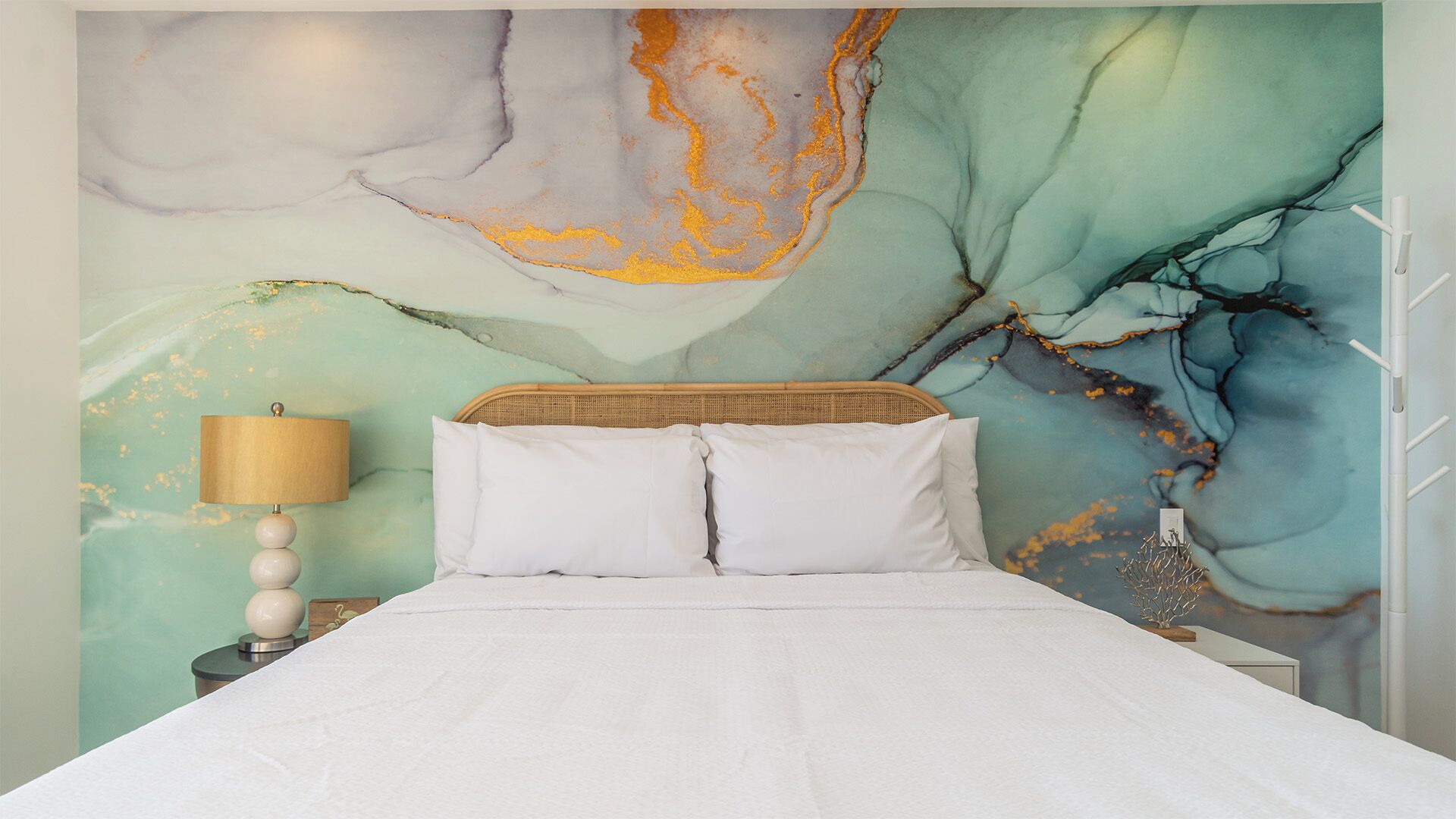 Une chambre à coucher avec un lit, du linge de lit blanc, une lampe et un mur orné d’œuvres d’art abstraites.