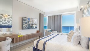 Une chambre d’hôtel moderne dotée d’un grand lit, d’un coin salon, d’une vue sur la mer et d’une fresque représentant un voilier.