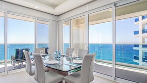 Un moderno comedor con una mesa de vidrio y sillas blancas, con vistas a un paisaje marino.