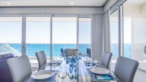 Un comedor con una mesa preparada para cuatro, ventanas amplias con vistas al mar y un balcón con vista al océano.