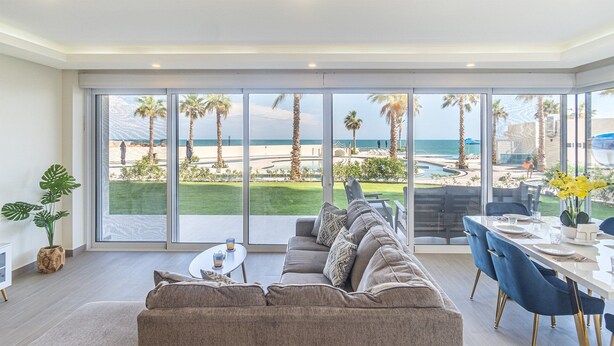 A modern living room with a large sliding glass door leading to a beach view. - Spectacular 2 Bedroom Ground Floor Condominium Encantame E 105 (Puerto Peñasco)