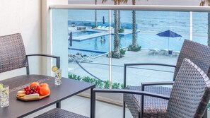 A balcony with a table set for two, overlooking a pool area with lounge chairs and palm trees. - Modern Luxury, Beachfront, Ocean Views C203 Encantame (Puerto Peñasco)