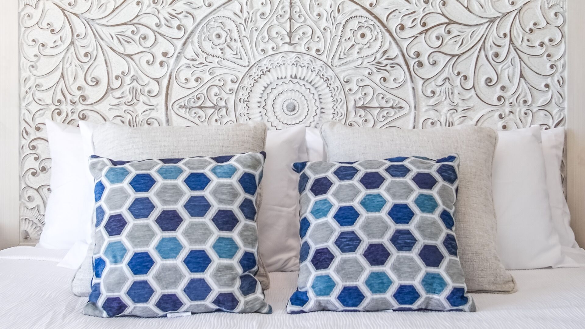A bed with two decorative pillows and a white headboard with intricate patterns.