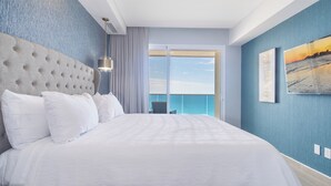 Habitación de hotel con una cama grande, vistas al océano y un balcón con una silla.