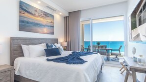 Ein modernes Hotelzimmer mit einem großen Bett, Meerblick, einem Balkon mit Sitzgelegenheit und einem Bild an der Wand.
