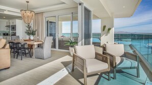 A modern interior with a dining area, a living room with a view of the ocean, and a balcony with a glass railing overlooking the sea.