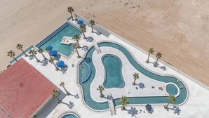 An aerial view of a resort with a large swimming pool, palm trees, and a beach area. - Encantame Towers Viento 1905 (Puerto Peñasco)