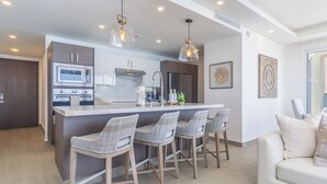 A modern kitchen with a central island, bar stools, a microwave, and a refrigerator. - Encantame Towers Viento 1905 (Puerto Peñasco)