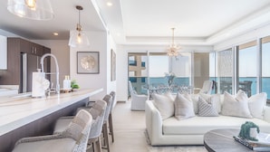 A modern living room with a white sofa, wicker chairs, and a dining area with a glass table. - Encantame Towers Viento 1905 (Puerto Peñasco)